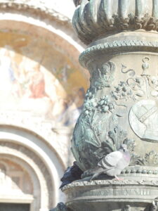 A pigeon sits on a lamp post in front of the entryway to St. Mark's Cathedral in Venice.