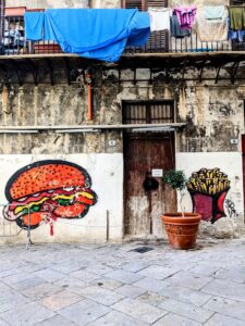 Street art in Sicily revels a burger and french fries with laundry drying on a balcony above.